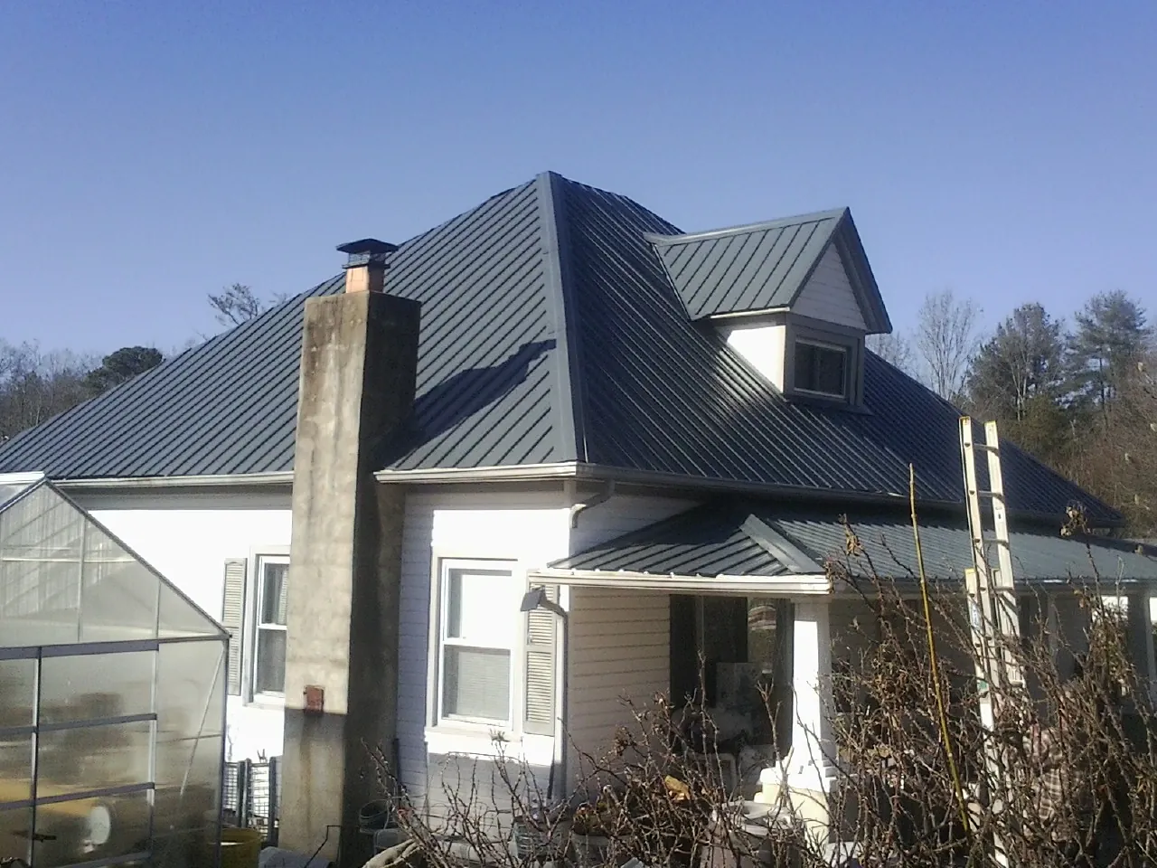 Dark blue standing seam metal roof on a white farmhouse with dormer — Slate & Tile Roof Repair by Roofing Brothers in Antonito