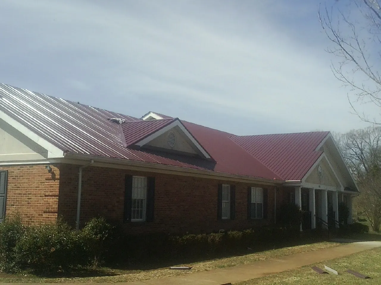 Red metal roof with gabled entries on a long brick building, from a Hail Damage Roof Repair job in Antonito