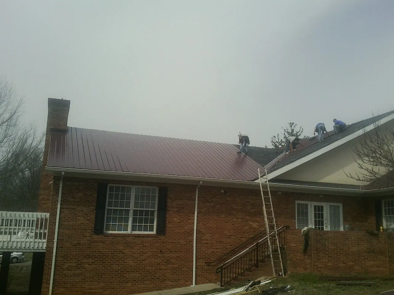 Crew setting red metal roofing panels on a brick home in Antonito