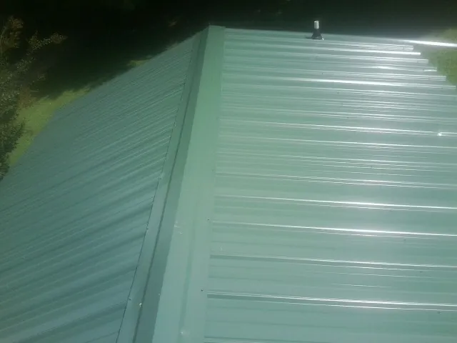 New green metal panels meeting at the ridge of a roof — Flat Roof Repair work by our crew in Antonito